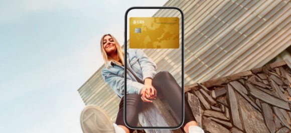 The image shows a woman sitting on a wall. Overlaying the scene is a transparent smartphone displaying a gold credit card in the digital wallet.