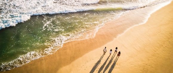 Overview of family group walking on the beach with a series of gentle waves.