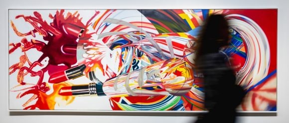 Bright colorful painting dominated by the color red with swirling patterns and the blurred figure of a person in front of the painting.