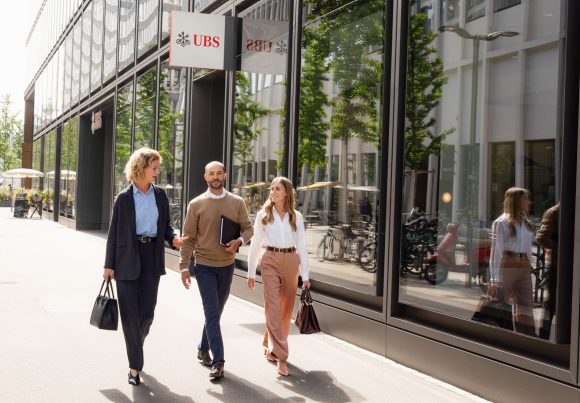 Three people walking along UBS offices