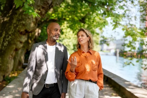 Two colleagues walking near the waterfront under trees
