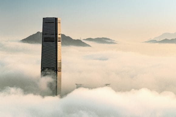 A tall skyscraper rises through dense clouds