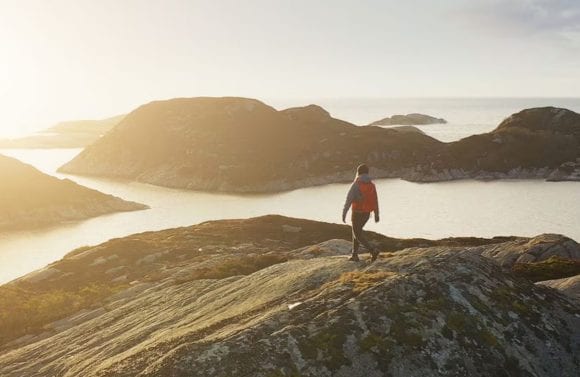 Man standing triumphantly at the mountain summit, bathed in beautiful sunshine