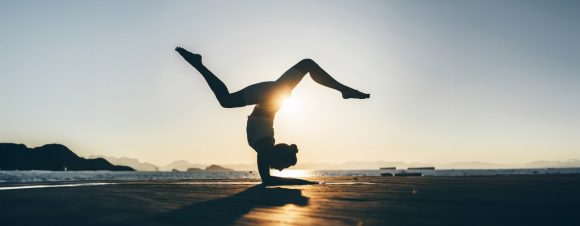 Woman on waterfront bordwalk at sunset performing yoga scorpion pose