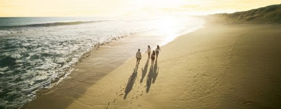 Aerial view of family walking along beach towards sunrise.