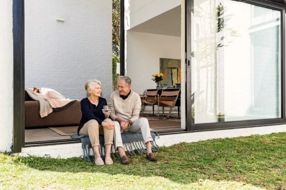 Älteres Paar sitzt auf der Schwelle zwischen Haus und Garten und unterhält sich.