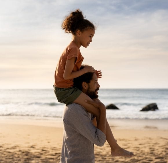 Vater trägt Tochter auf seinen Schultern am Strand.