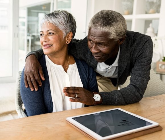 Älteres Paar sitzt nebeneinander am Tisch und schaut lächelnd in die Ferne.
