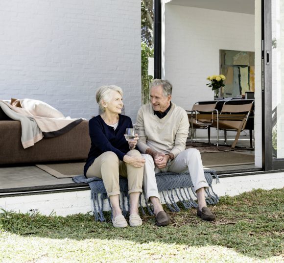Mature couple sitting in front of an open patio door and chatting.