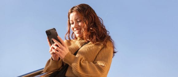 Red-haired woman in ochre sweater smiling at a smartphone