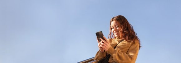 Red-haired woman in ochre sweater smiling at a smartphone