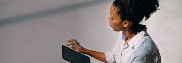 Black woman with curly hair in a bun sitting and holding a tablet