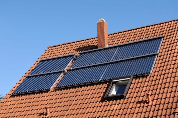 Solar panels on a red tiled roof of a residential building, blue sky above.