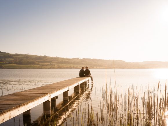 Man and woman sitting on pier at lake.