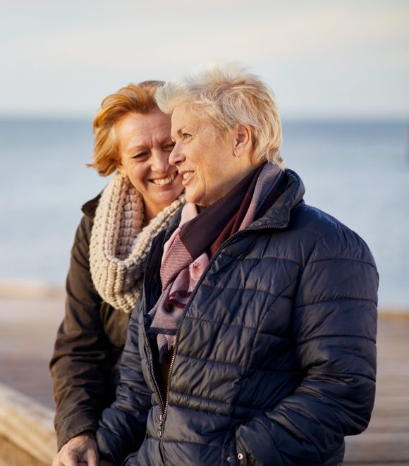 Two women laughing and talking by the sea.