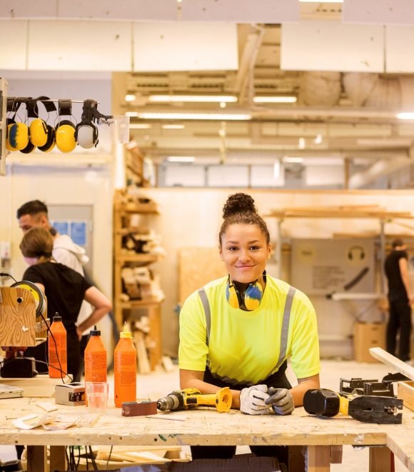 Une femme en tenue de travail s’appuie sur une table.