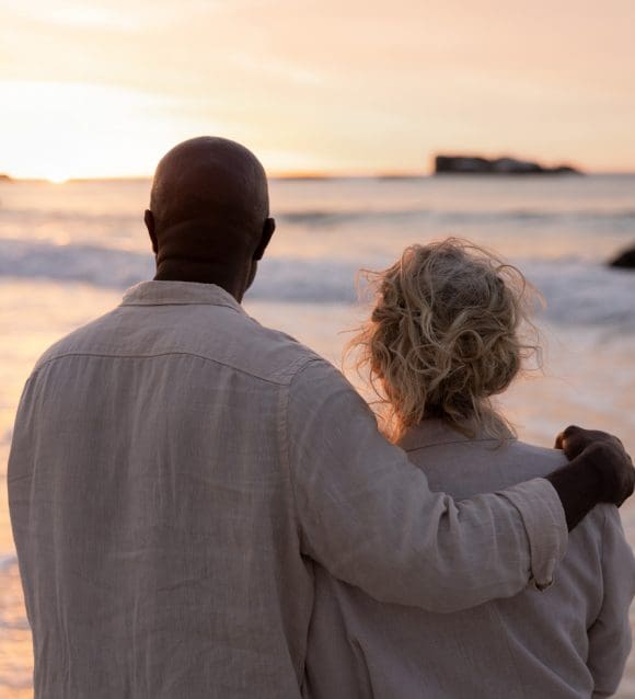 Un couple âgé regarde le coucher de soleil sur la plage (vue de dos).