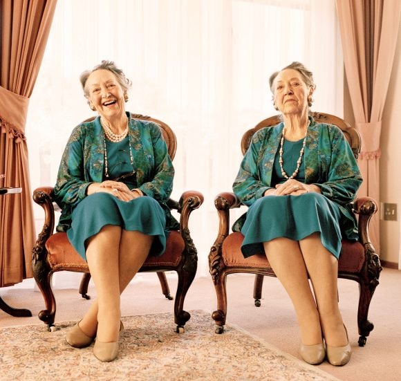 Two similar-looking women are sitting on chairs next to each other.