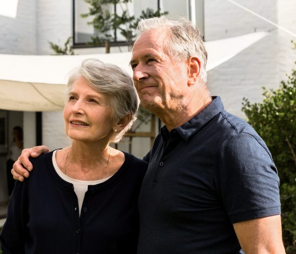 Un couple âgé se tient dans le jardin devant sa maison.