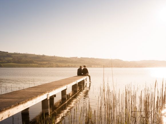 Homme et femme assis sur une jetée au bord d’un lac.