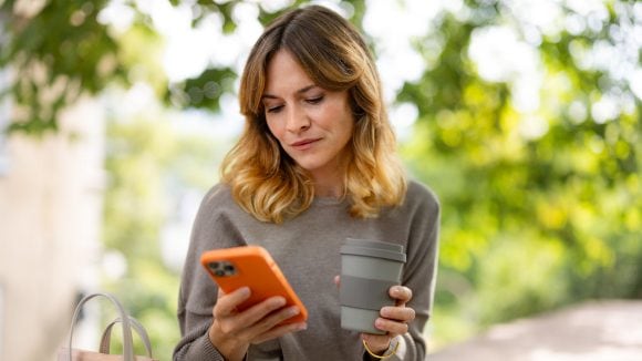 Une femme tient son café d’une main et consulte son smartphone de l’autre.