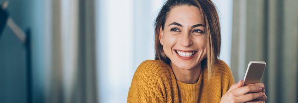 Happy woman sitting with a smartphone over a cup