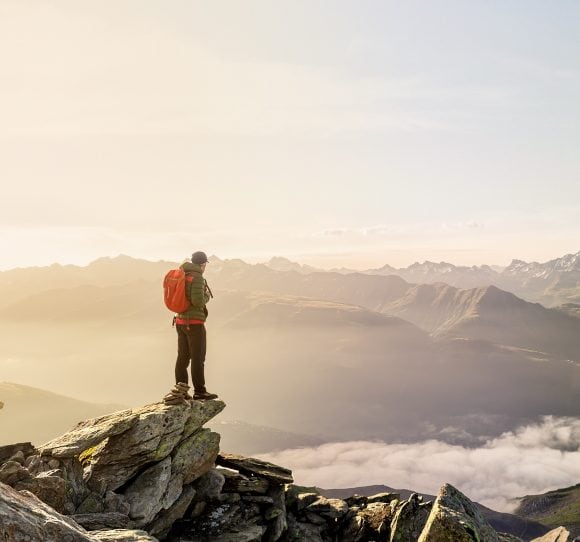 L’escursionista si trova sulla cima di una montagna e può osservare la catena montuosa che si erge sopra le nuvole.