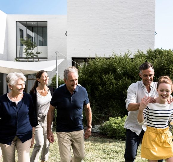 Genitori, nonni e una figlia camminano sorridendo nel giardino di una casa.