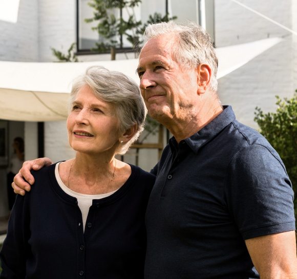 Coppia di anziani in piedi nel giardino di fronte alla loro casa.