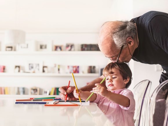 Nonno e nipote disegnano assieme seduti attorno un tavolo.