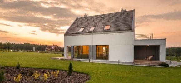 Auf dem Bild sieht man ein Einfamilienhaus auf einer grünen Wiese im Sonnenuntergang.