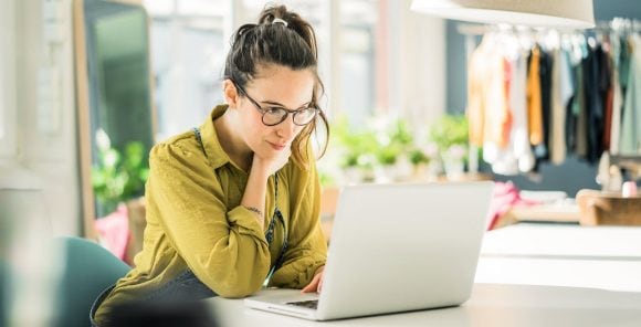 A woman sits outside at a wooden table in the evening sun and is researching early retirement on her laptop.