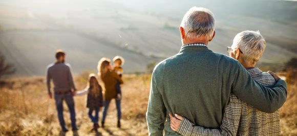 Old couple hanging and seeing the young family with father, mother and children at a sunny field.