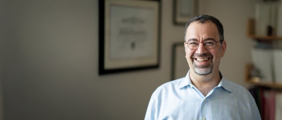 A portrait of the Turkish-American economist Daron Acemoglu with a library in the background.