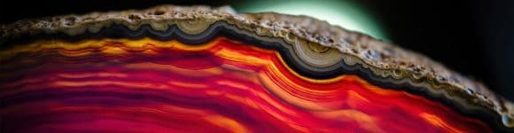 Abstract close-up of layered, agate-like bands in vivid red, orange and pink