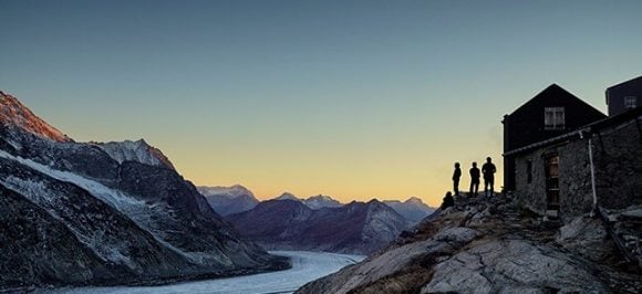 L’image montre des personnes au sommet d’une montagne regardant le lever du soleil sur un glacier.