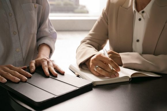 Two people engaged in a discussion, tablet and notebook in hand.