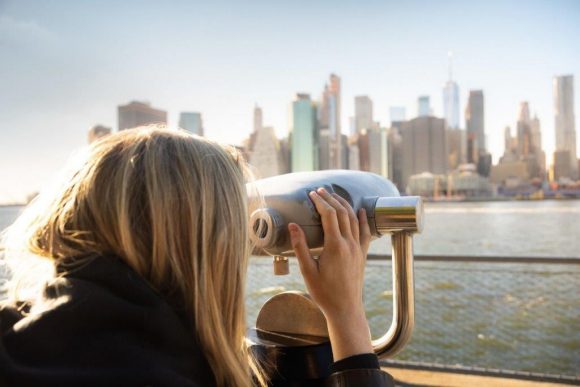 A female looking at the city skyline through a telescope