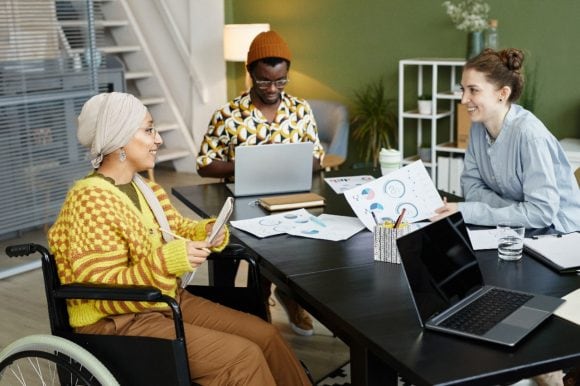 Woman on a wheelchair smiling and discussing with her male colleague in the training room.
