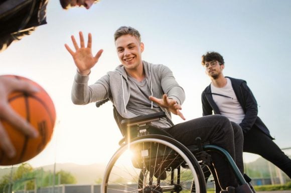 Three friends playing basketball, one of them on a wheelchair