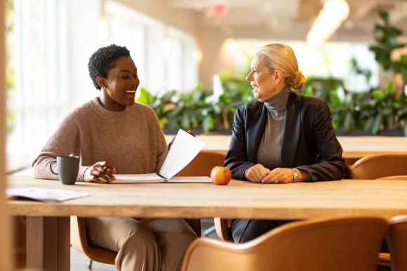 Two women at a wooden table smiling and talking