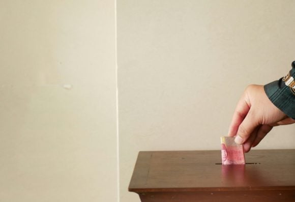 A hand drops notes into a fundraising collection box