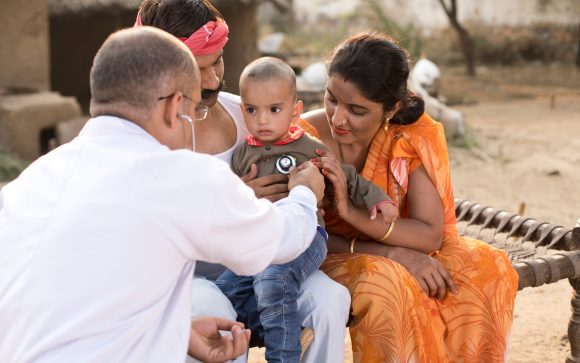 Male medical professional engaging with a mother and child in an outdoor community setting
