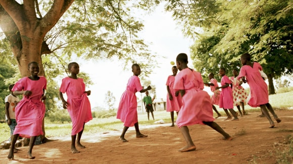 Happy girls in vibrant pink dresses dancing barefoot under a large tree