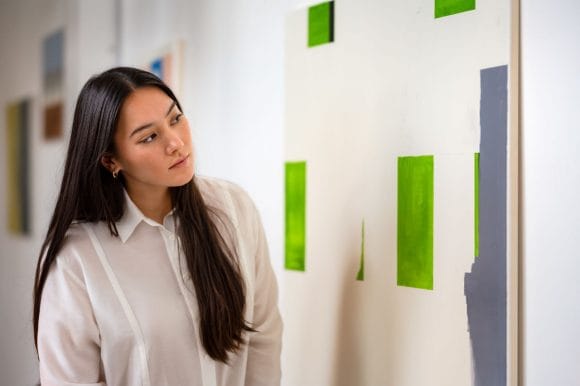 Asian woman looking closely at picture in modern art gallery