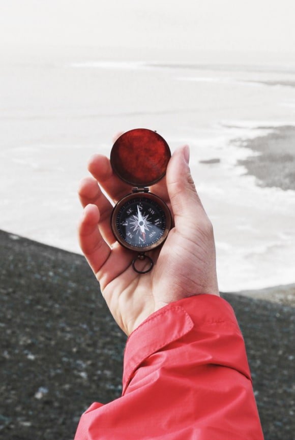 Una mano sosteniendo una brújula con el océano en la distancia