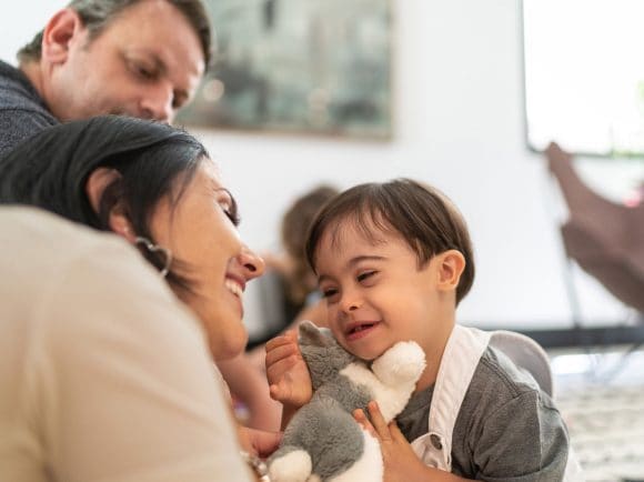 A mother and a father smiling at a young child holding a teddy bear