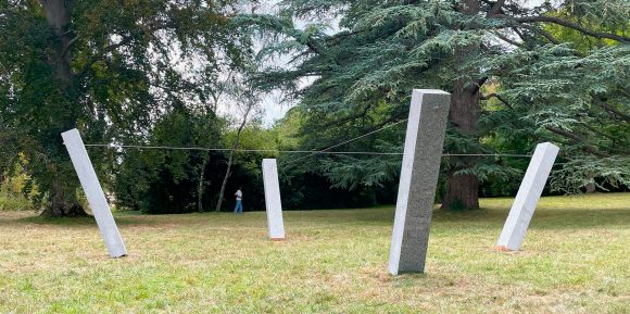 Quatre stèles de granit inclinées vers l'arrière, reliées en croix par deux câbles d'acier (Œuvre d'art in situ « Spalla » de Simon Deppierraz)