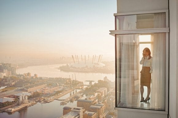 A woman with a phone stands on balcony of the high rise building