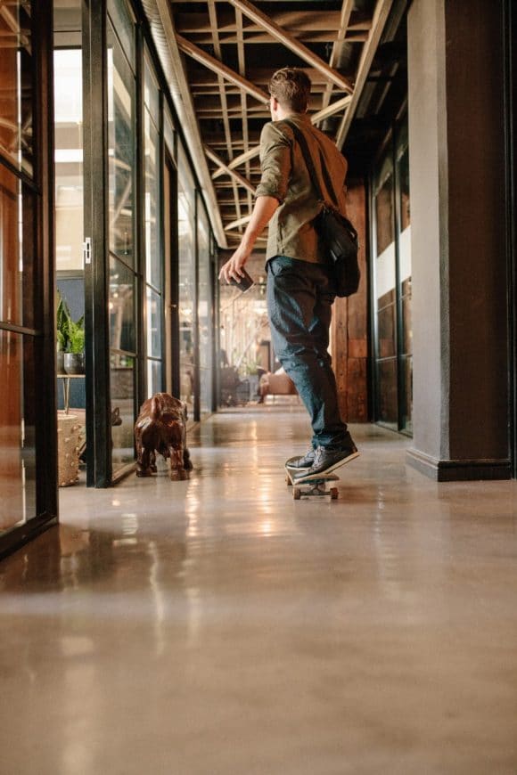 Young businessman riding on skateboard past a corporate building.